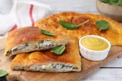 Photo of Tasty calzones with basil, cheese and sauce on white wooden table, closeup