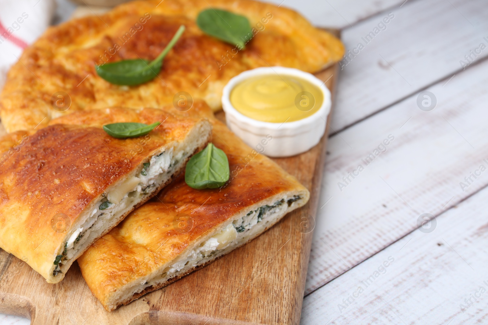 Photo of Tasty calzones with basil, cheese and sauce on white wooden table, closeup. Space for text