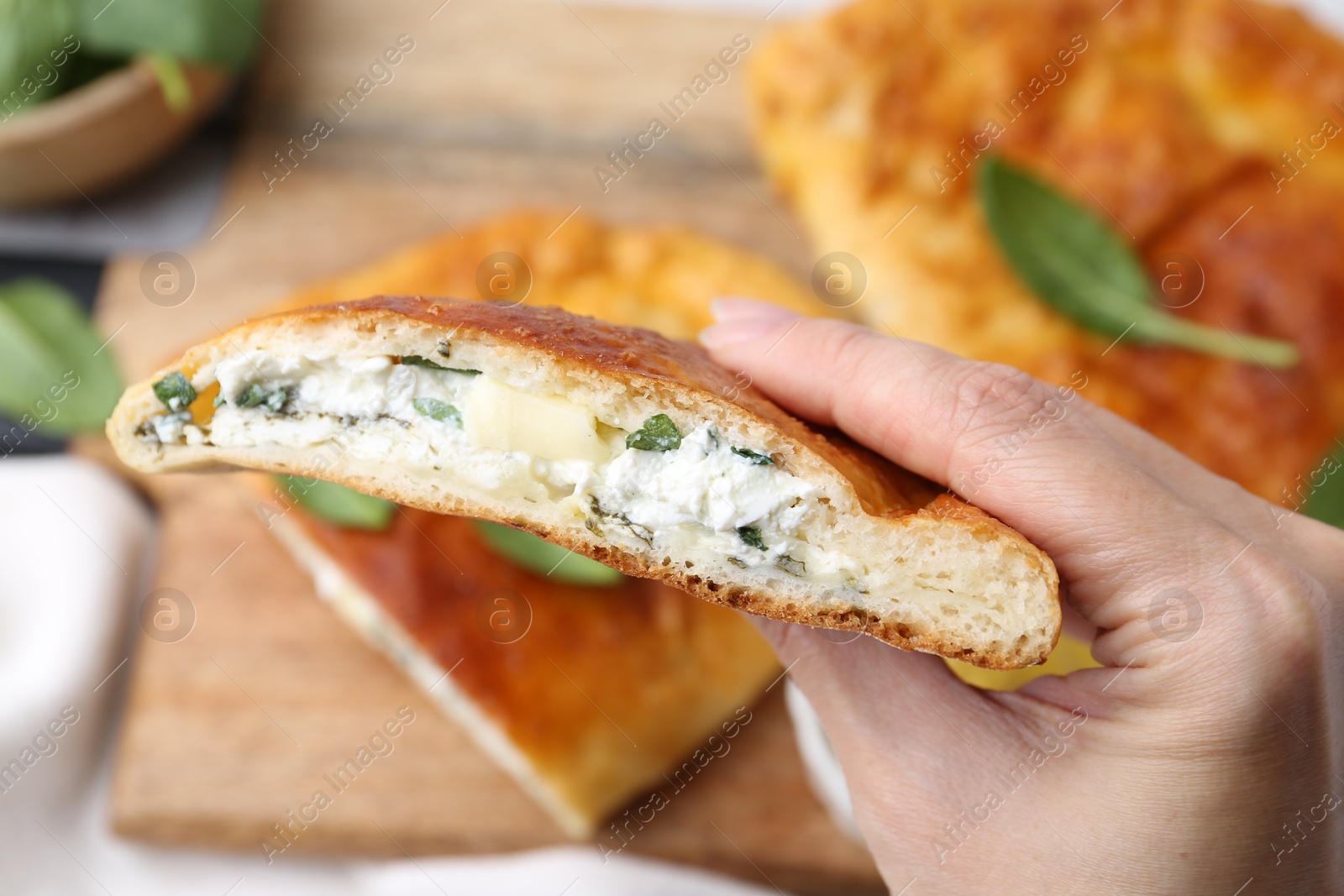 Photo of Woman holding piece of tasty with basil and cheese on blurred background, closeup