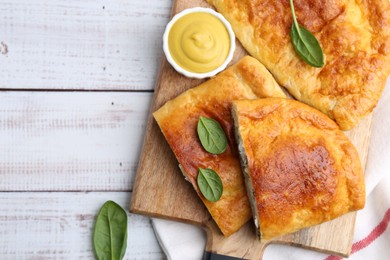 Photo of Tasty calzones with basil, cheese and sauce on white wooden table, top view. Space for text