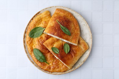 Photo of Tasty calzones with basil and cheese on white tiled table, top view