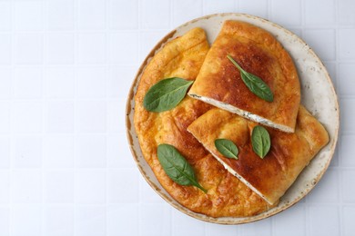 Tasty calzones with basil and cheese on white tiled table, top view. Space for text