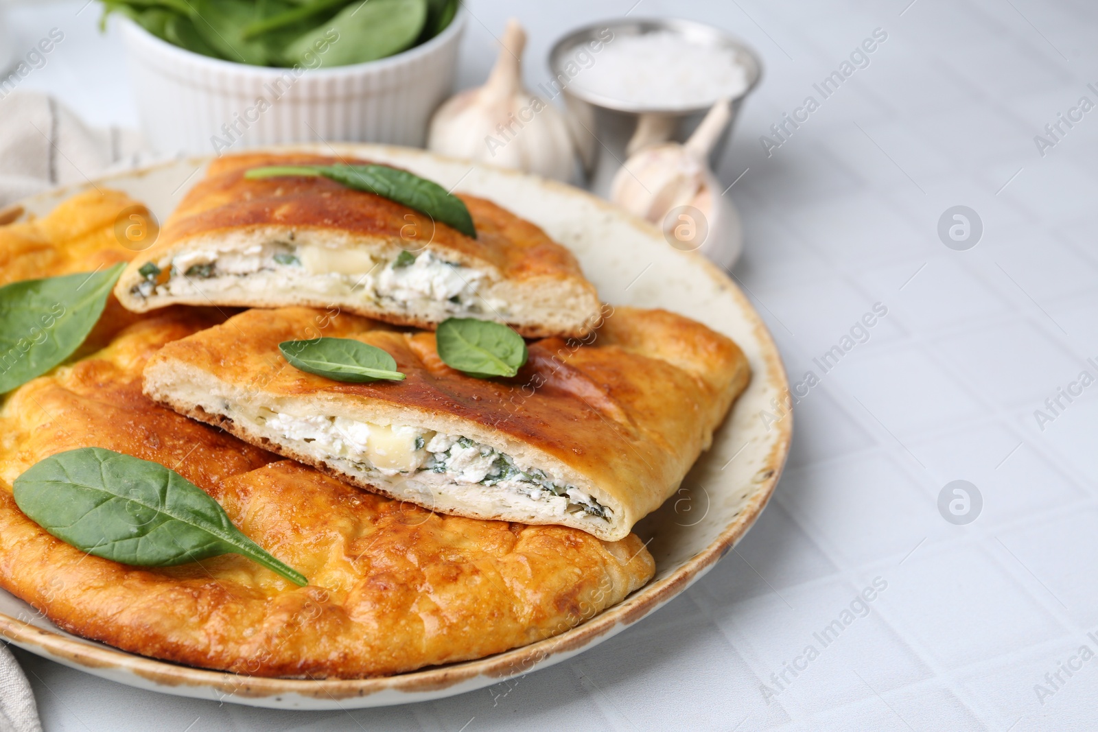 Photo of Tasty calzones with basil and cheese on white tiled table, closeup. Space for text