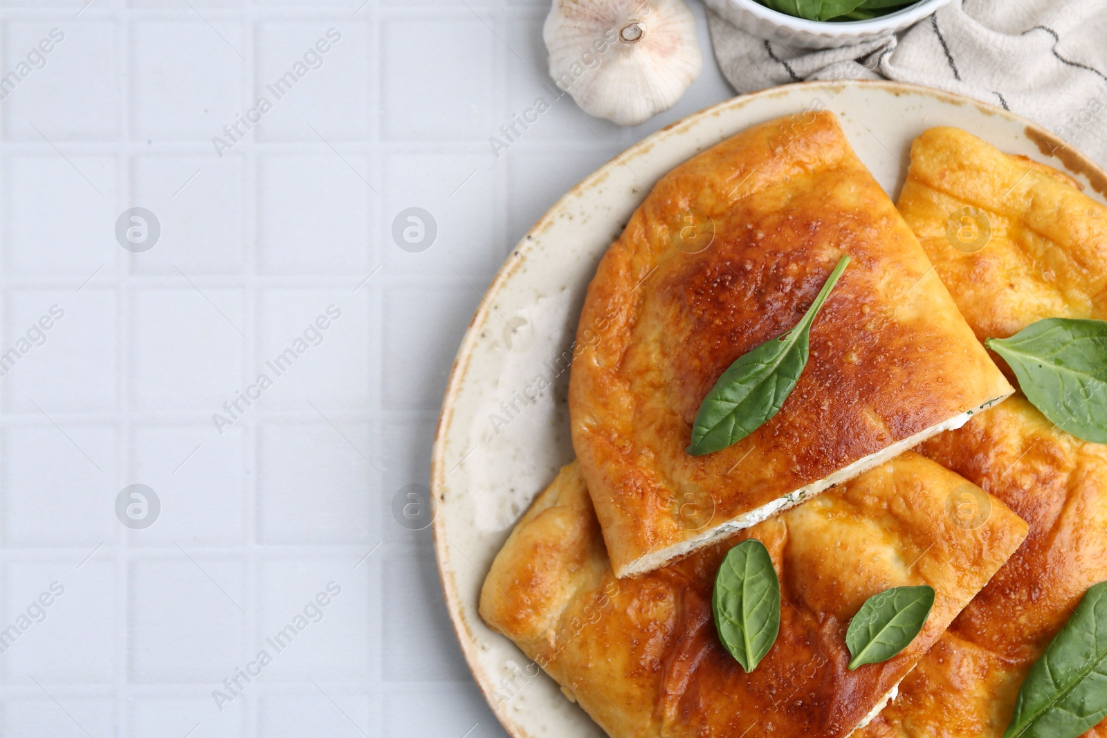 Photo of Tasty calzones with basil and cheese on white tiled table, top view. Space for text