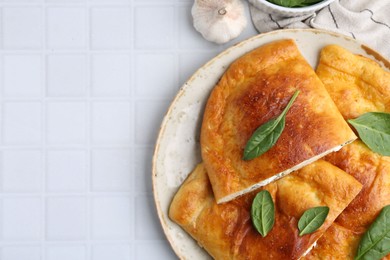 Photo of Tasty calzones with basil and cheese on white tiled table, top view. Space for text