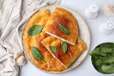 Tasty calzones with basil and cheese on white tiled table, flat lay