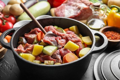 Photo of Cooking stew. Uncooked meat, vegetables and pot on black table