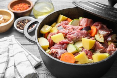 Photo of Cooking stew. Uncooked meat and vegetables in pot on light grey wooden table, closeup