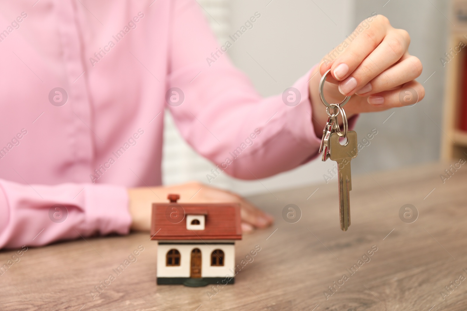 Photo of Real estate agent with house model and key at wooden table, closeup