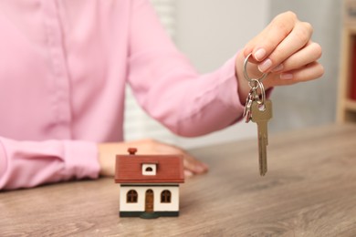 Photo of Real estate agent with house model and key at wooden table, closeup