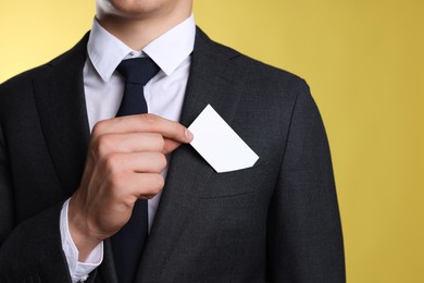 Photo of Man taking blank business card from pocket of his jacket on yellow background, closeup. Mockup for design