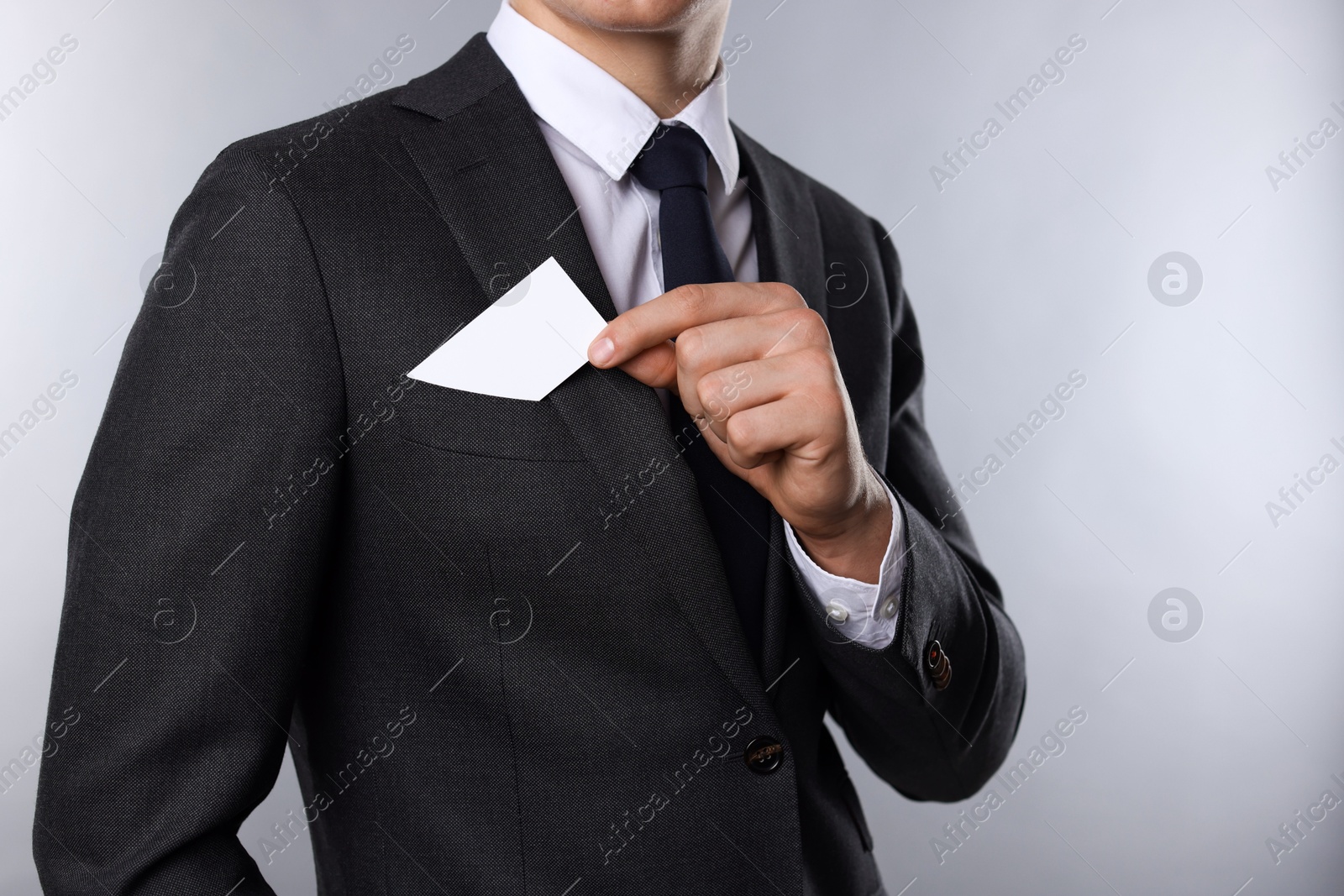 Photo of Man taking blank business card from pocket of his jacket on grey background, closeup. Mockup for design