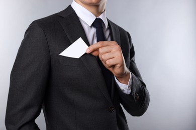 Man taking blank business card from pocket of his jacket on grey background, closeup. Mockup for design