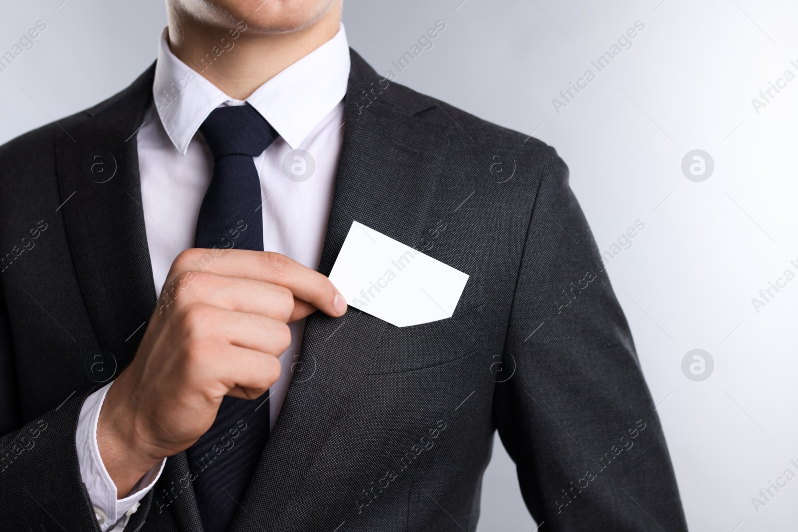 Photo of Man taking blank business card from pocket of his jacket on grey background, closeup. Mockup for design