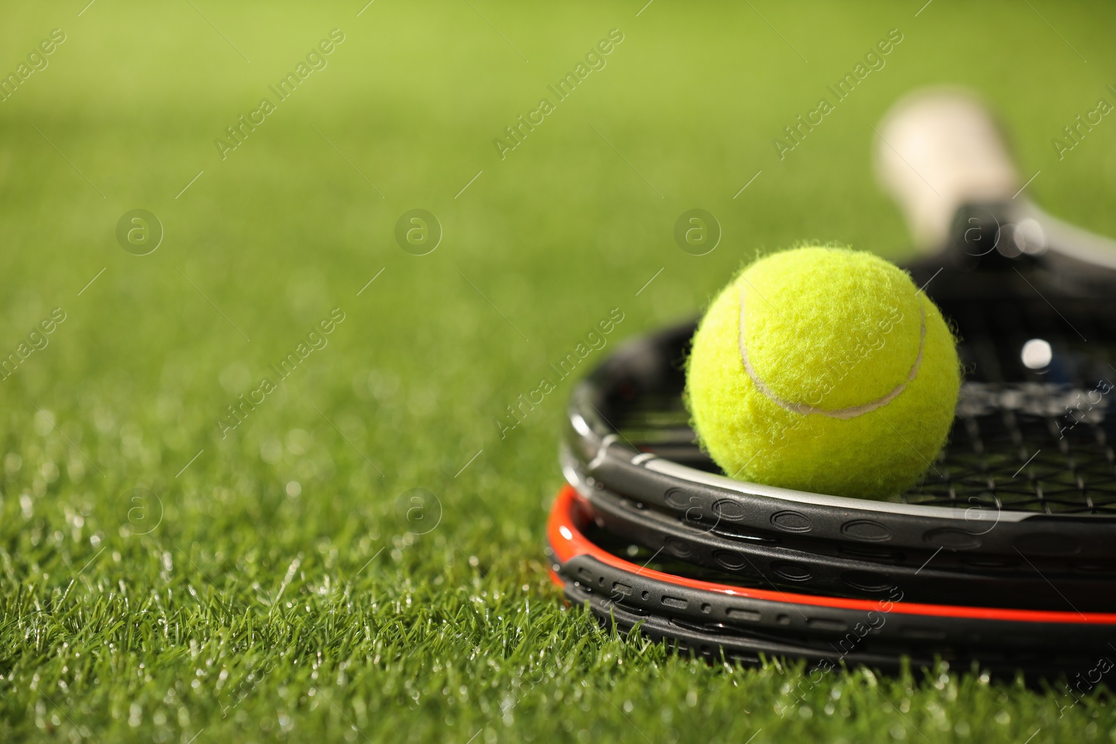 Photo of Tennis rackets and ball on green artificial grass, closeup. Space for text