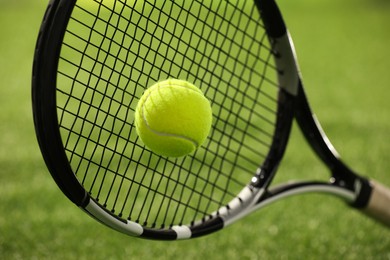 Tennis racket with ball on green artificial grass, closeup