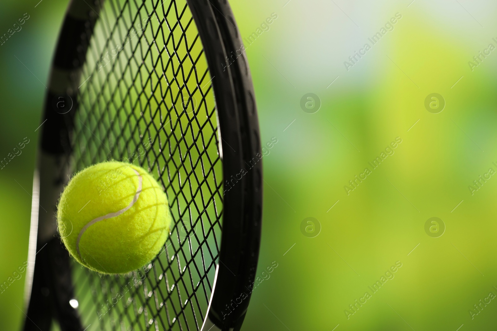 Photo of Tennis racket with ball against blurred green background, closeup. Space for text