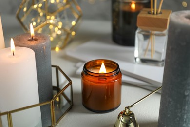 Photo of Beautiful burning candles on light table against blurred lights, closeup