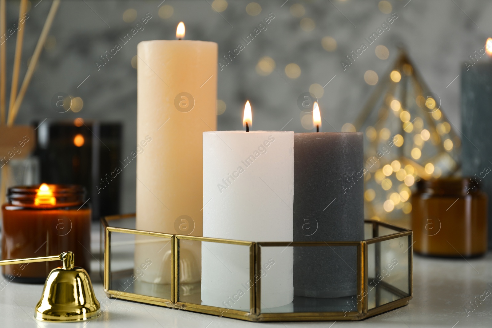 Photo of Beautiful burning candles on light table against blurred lights, closeup