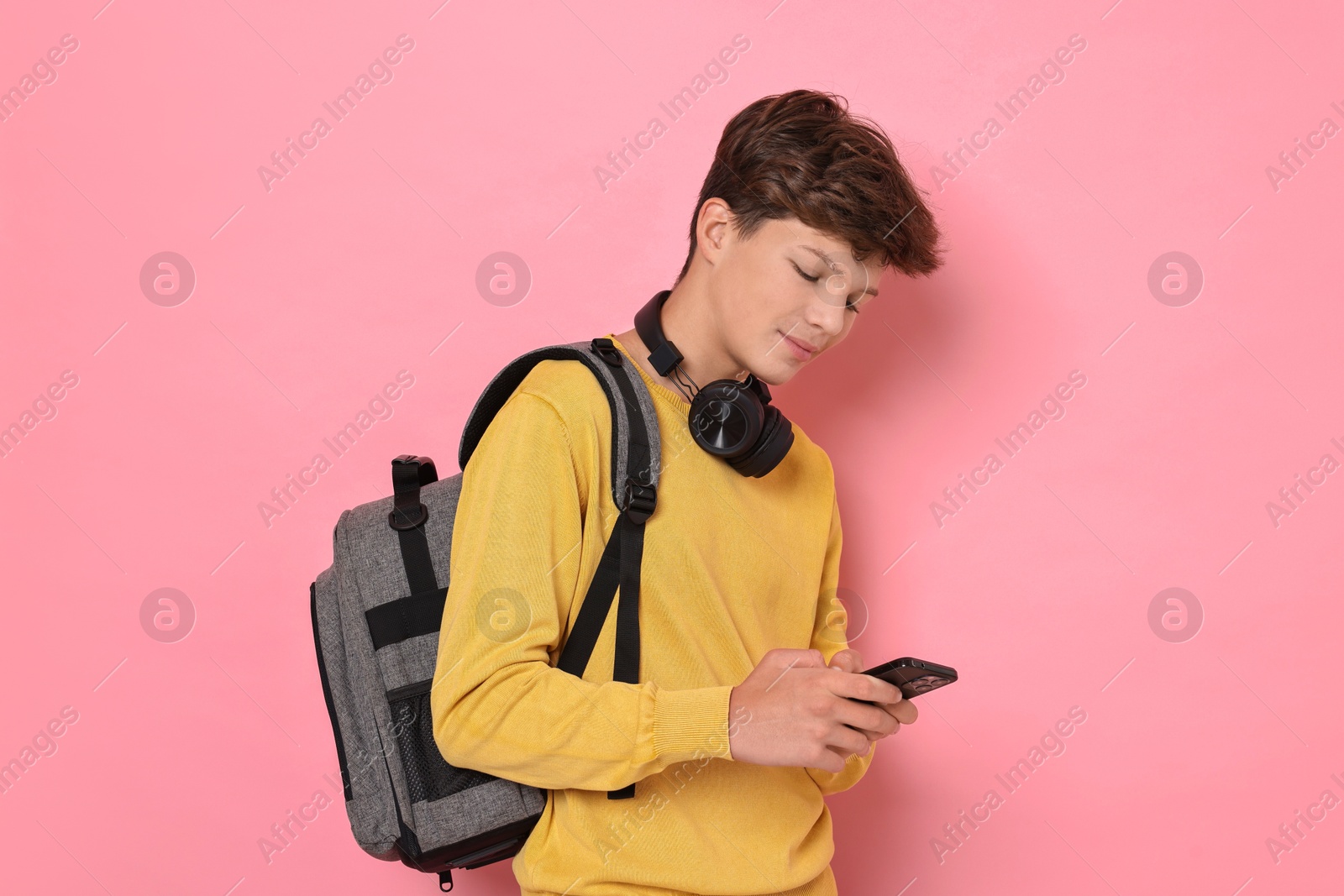 Photo of Teenage boy with headphones, smartphone and backpack on pink background