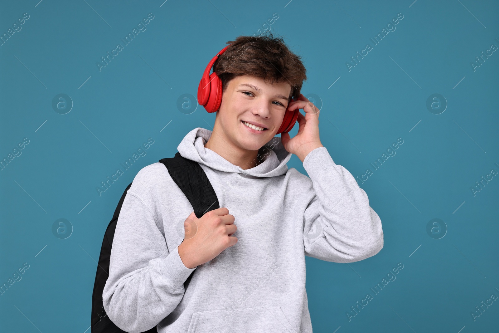 Photo of Teenage boy in headphones with backpack on light blue background