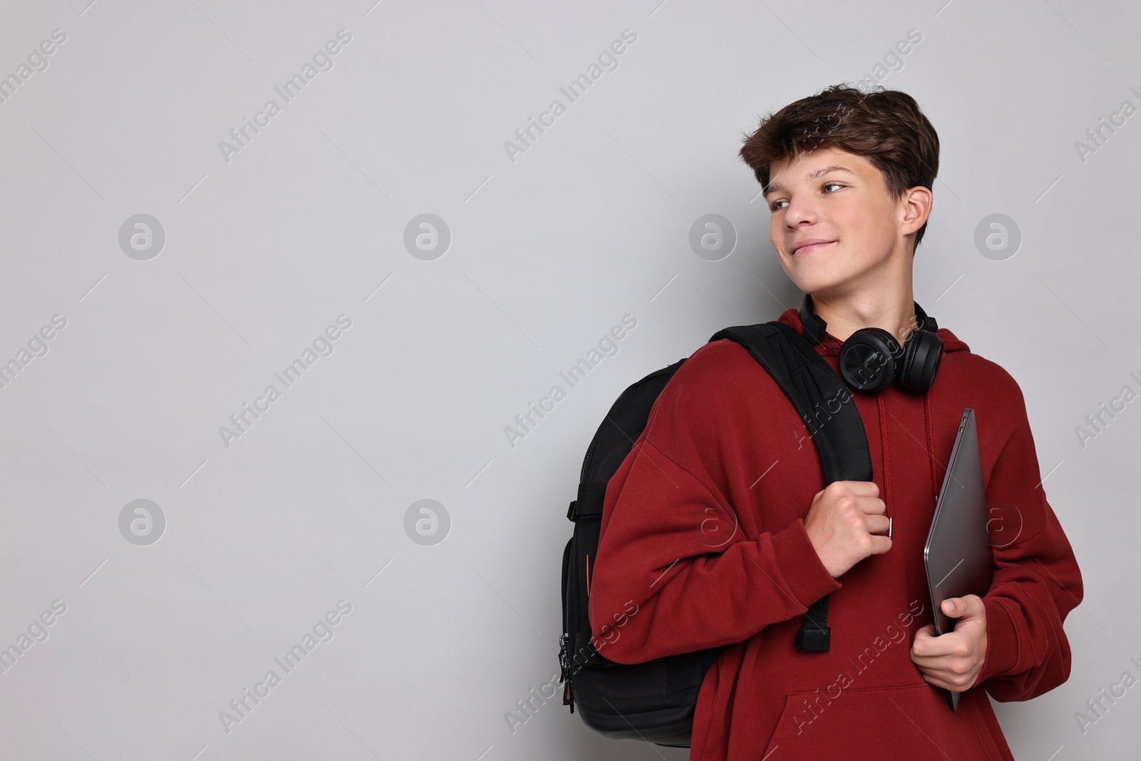 Photo of Teenage boy with headphones, laptop and backpack on light grey background, space for text