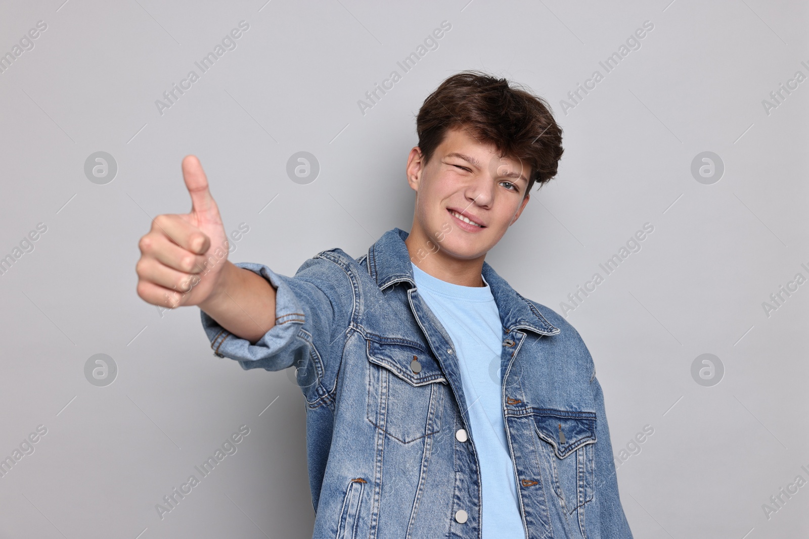 Photo of Happy teenage boy showing thumbs up on light grey background