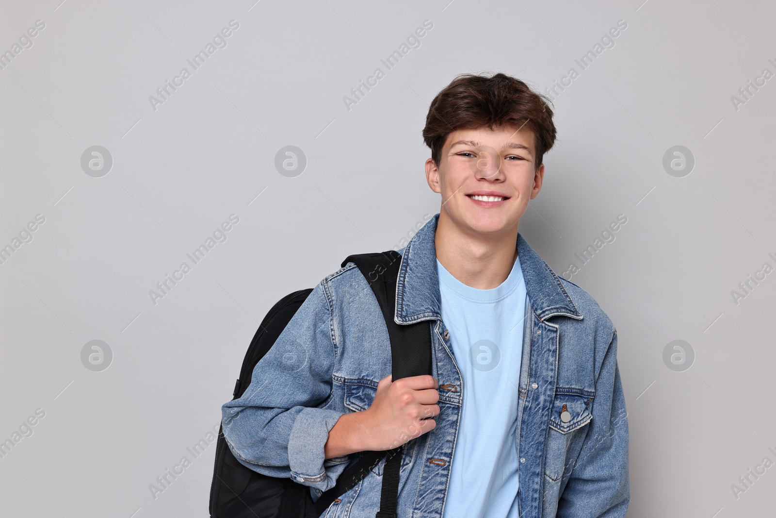 Photo of Happy teenage boy with backpack on light grey background