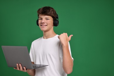 Photo of Teenage boy in headphones with laptop on green background, space for text