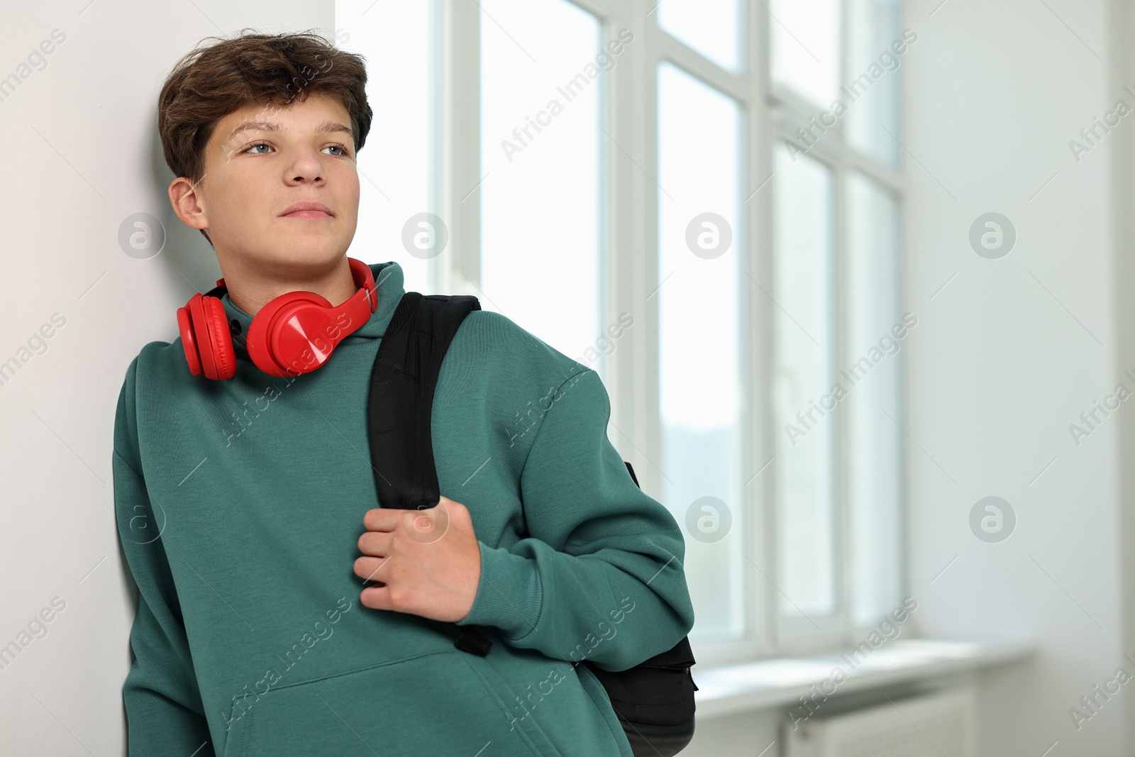 Photo of Teenage boy with headphones and backpack indoors, space for text