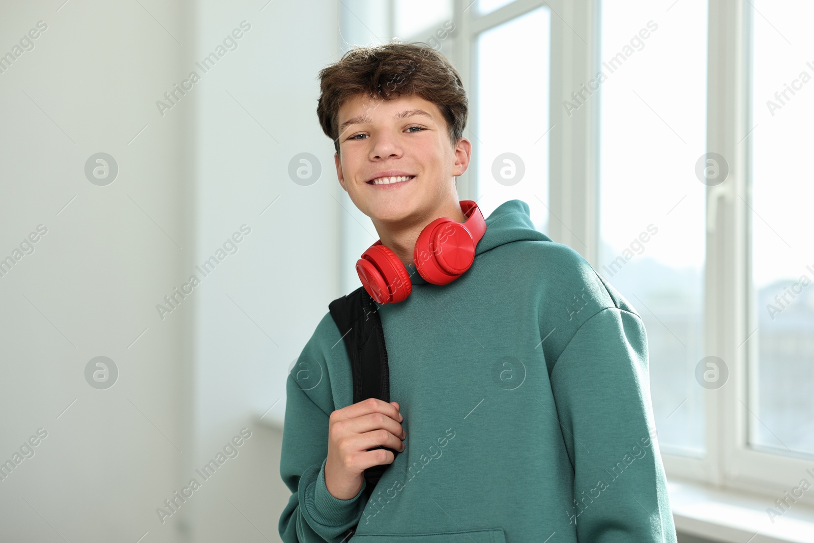 Photo of Happy teenage boy with headphones and backpack indoors