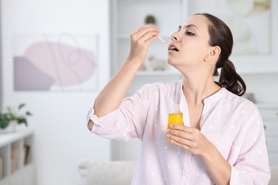 Photo of Young woman taking CBD tincture indoors. Herbal extract