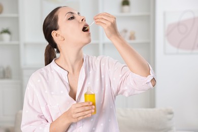 Photo of Young woman taking CBD tincture indoors. Herbal extract