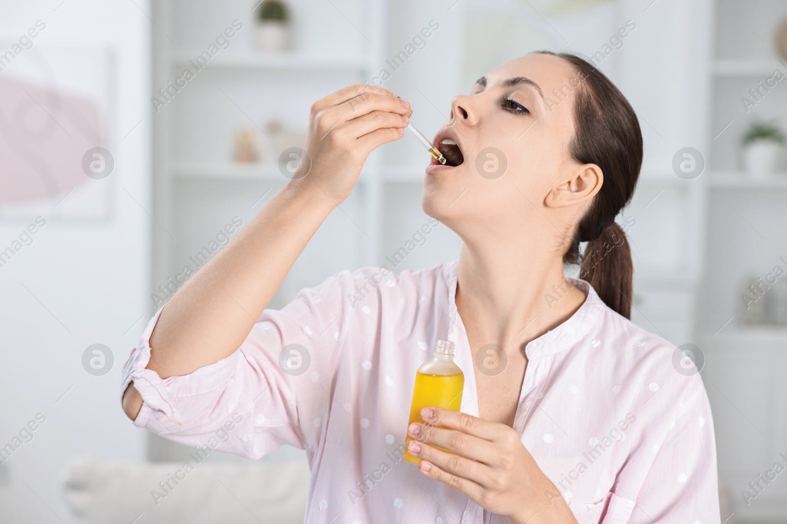 Photo of Young woman taking CBD tincture indoors. Herbal extract