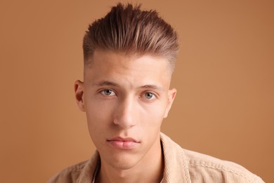 Photo of Confident young man with stylish haircut on brown background