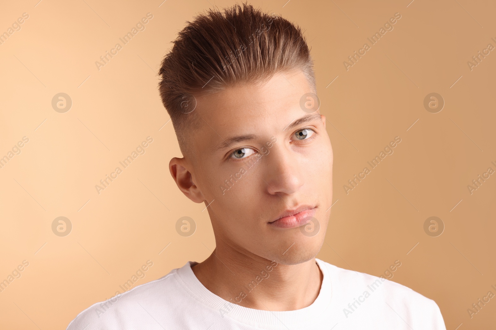 Photo of Confident young man with stylish haircut on light brown background