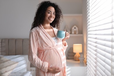 Photo of Portrait of beautiful pregnant with cup of drink near window at home