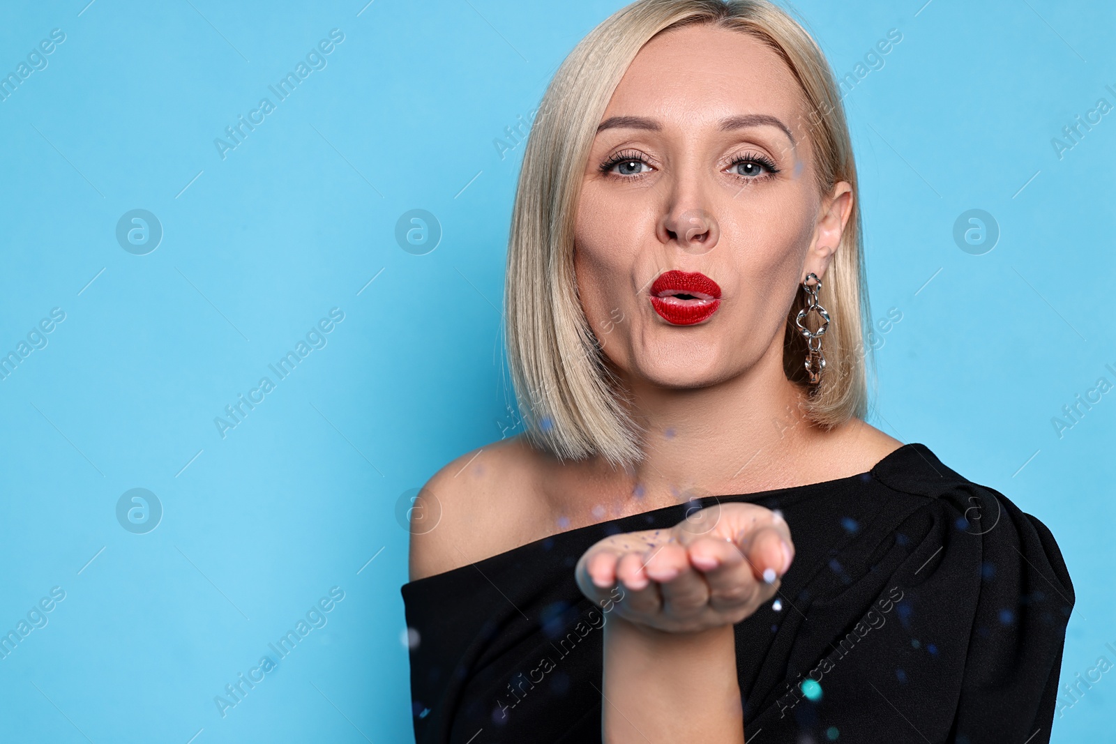 Photo of Woman with perfect makeup blowing confetti on light blue background. Space for text