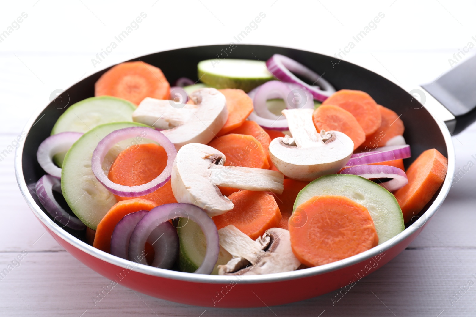 Photo of Frying pan with mix of fresh vegetables and mushrooms on white wooden table, closeup