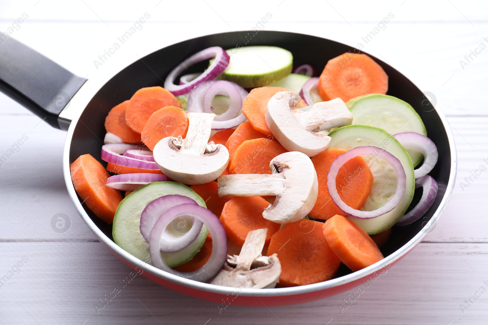 Photo of Frying pan with mix of fresh vegetables and mushrooms on white wooden table, closeup