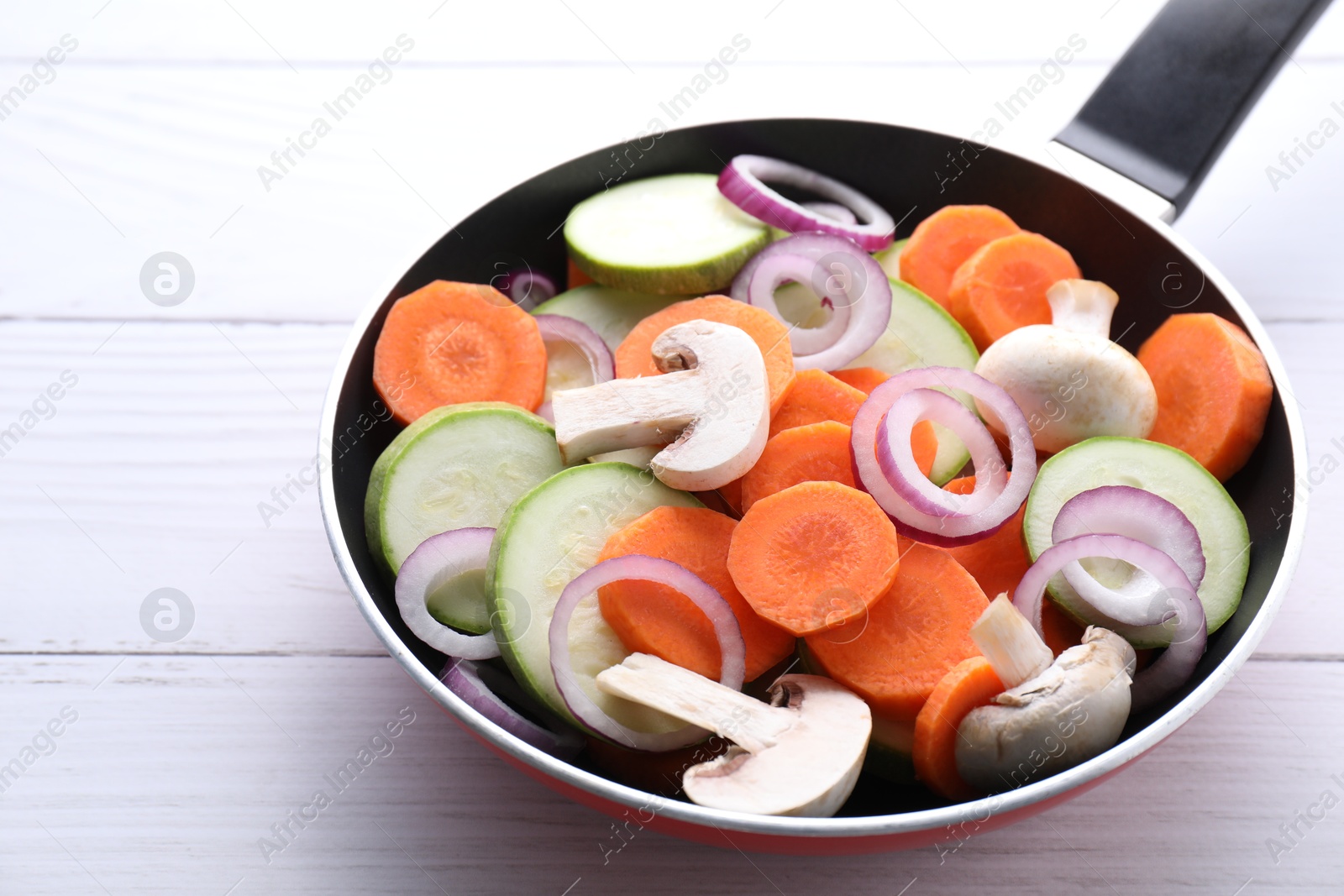 Photo of Frying pan with mix of fresh vegetables and mushrooms on white wooden table, closeup