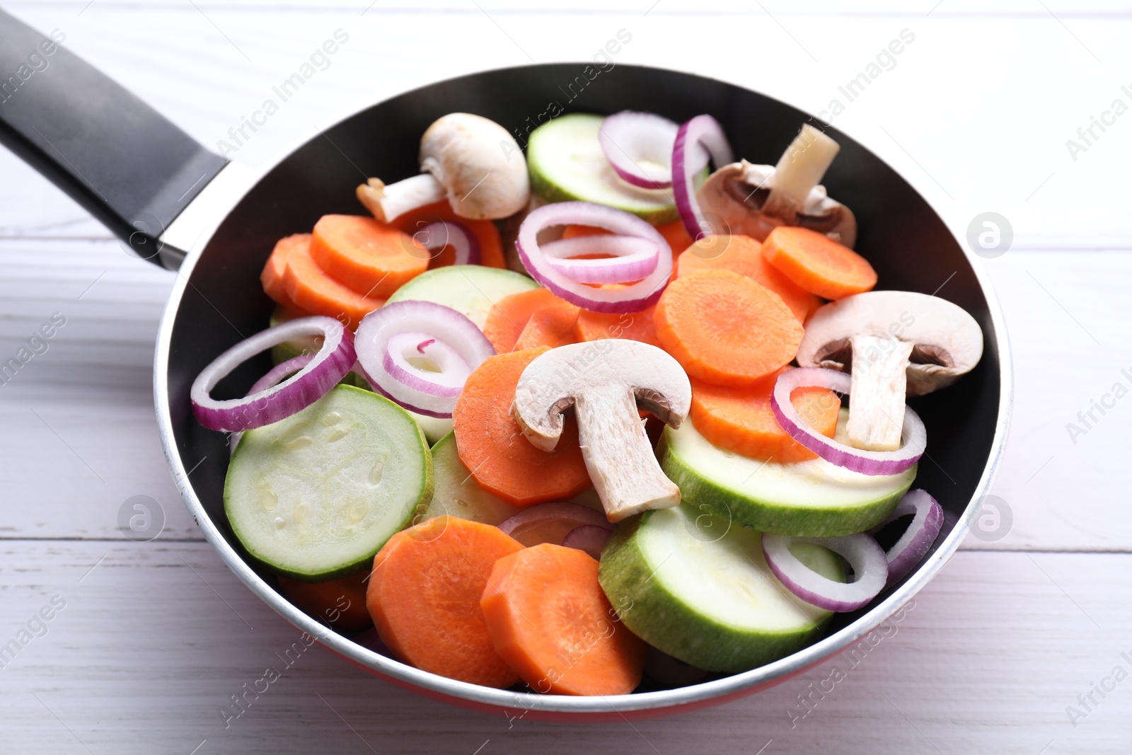 Photo of Frying pan with mix of fresh vegetables and mushrooms on white wooden table, closeup