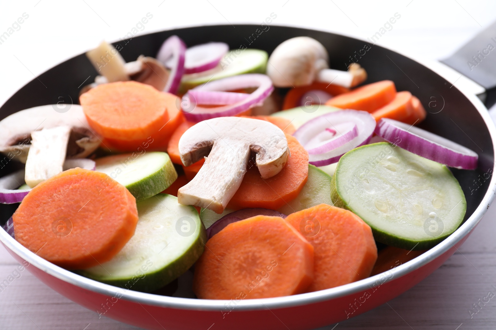 Photo of Frying pan with mix of fresh vegetables and mushrooms on white wooden table, closeup