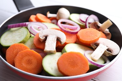 Photo of Frying pan with mix of fresh vegetables and mushrooms on white wooden table, closeup