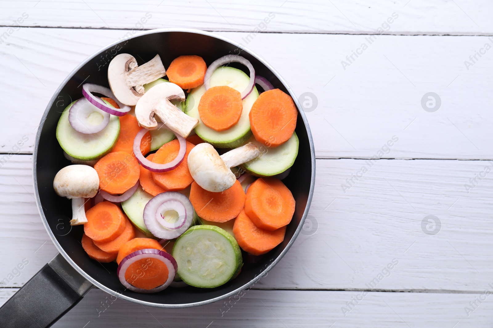 Photo of Frying pan with mix of fresh vegetables and mushrooms on white wooden table, top view. Space for text