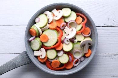 Photo of Frying pan with mix of fresh vegetables and mushrooms on white wooden table, top view