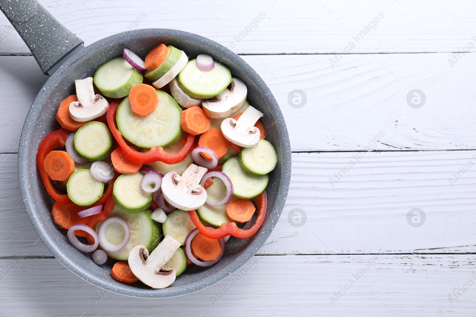 Photo of Frying pan with mix of fresh vegetables and mushrooms on white wooden table, top view. Space for text