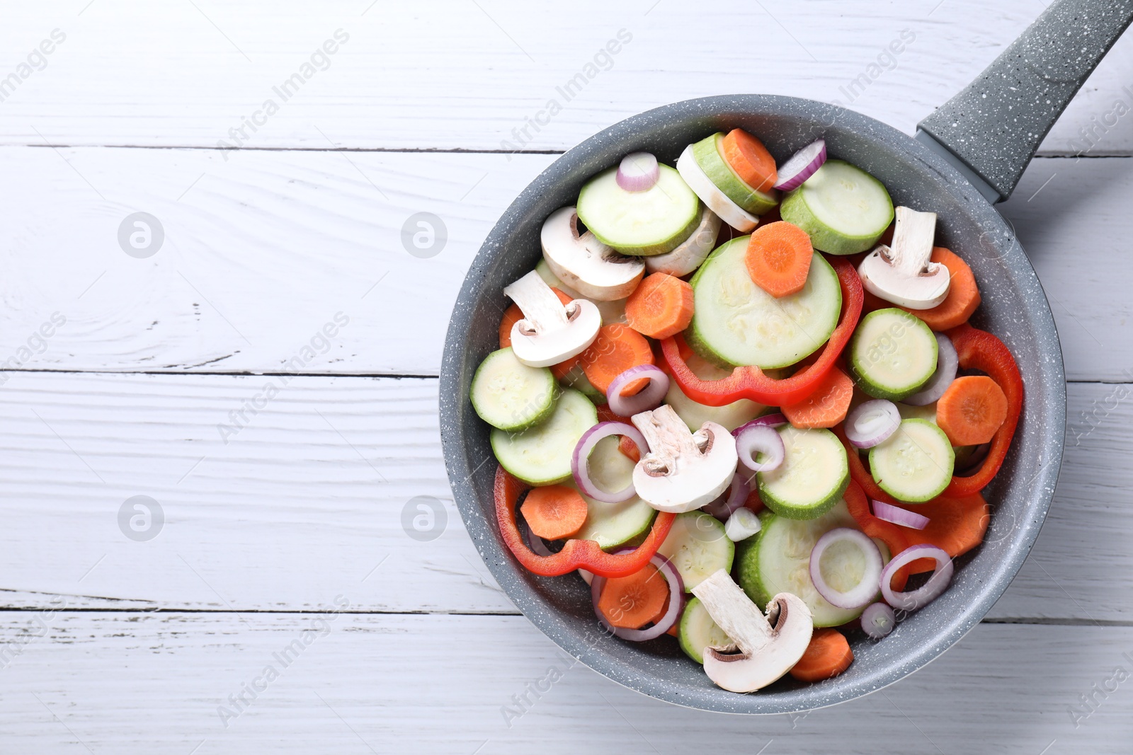 Photo of Frying pan with mix of fresh vegetables and mushrooms on white wooden table, top view. Space for text