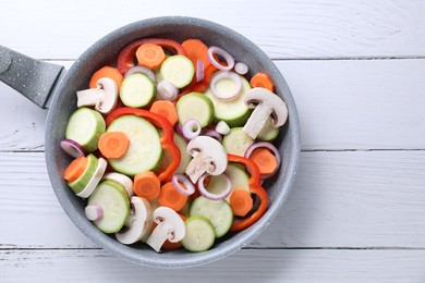 Photo of Frying pan with mix of fresh vegetables and mushrooms on white wooden table, top view