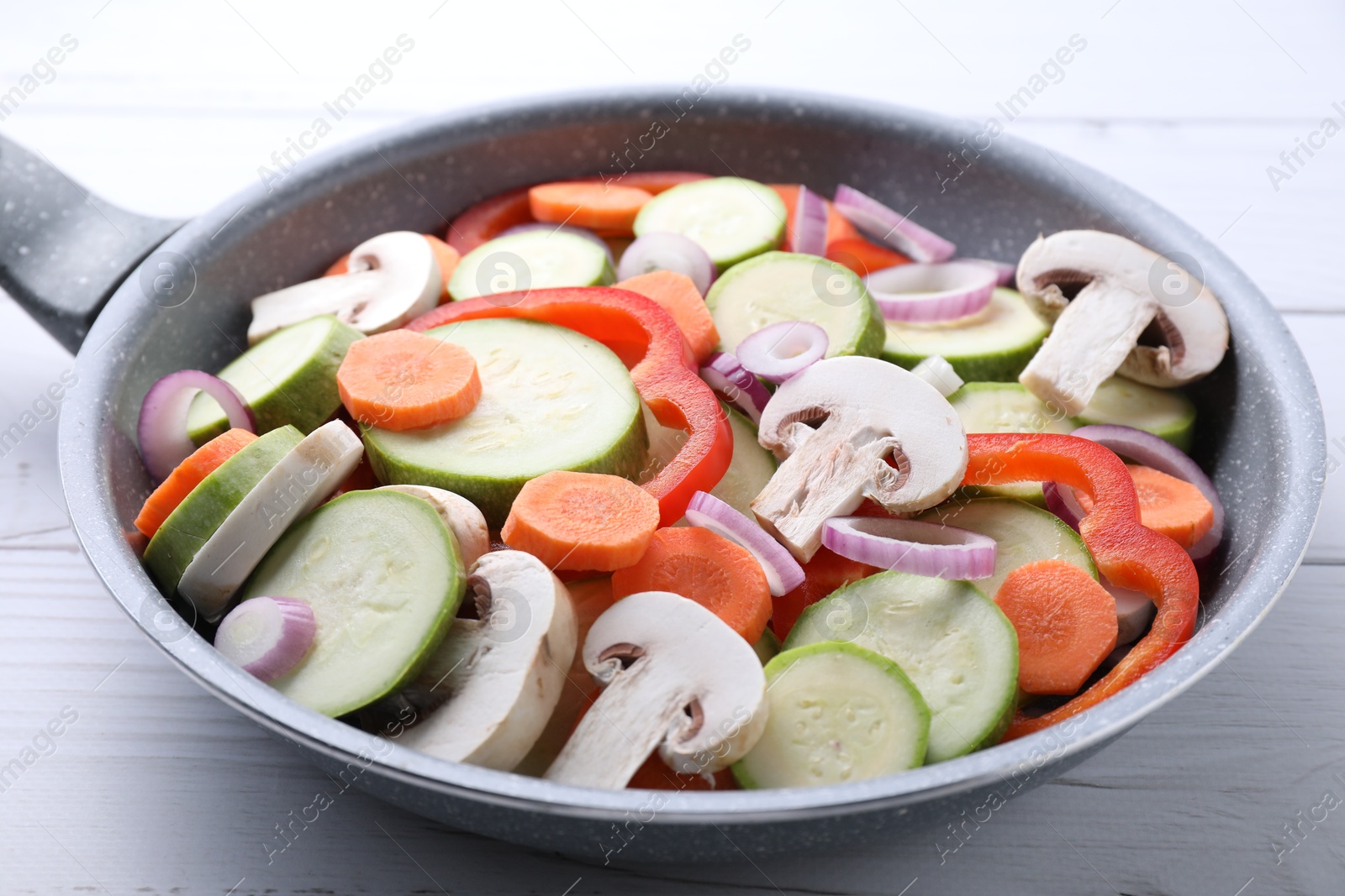 Photo of Frying pan with mix of fresh vegetables and mushrooms on white wooden table, closeup